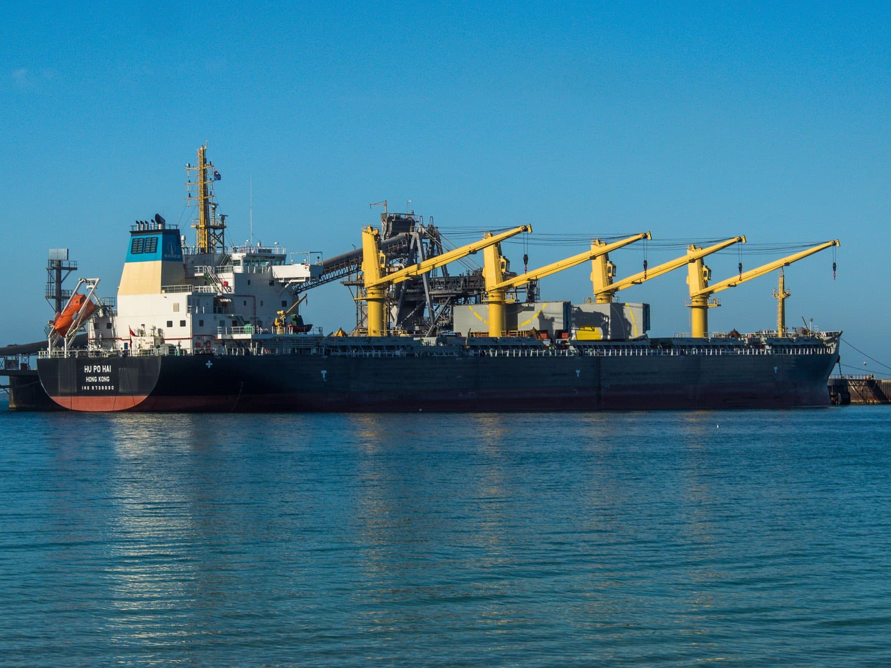 A geared bulk carrier lying alongside a berth with its cranes stowed.