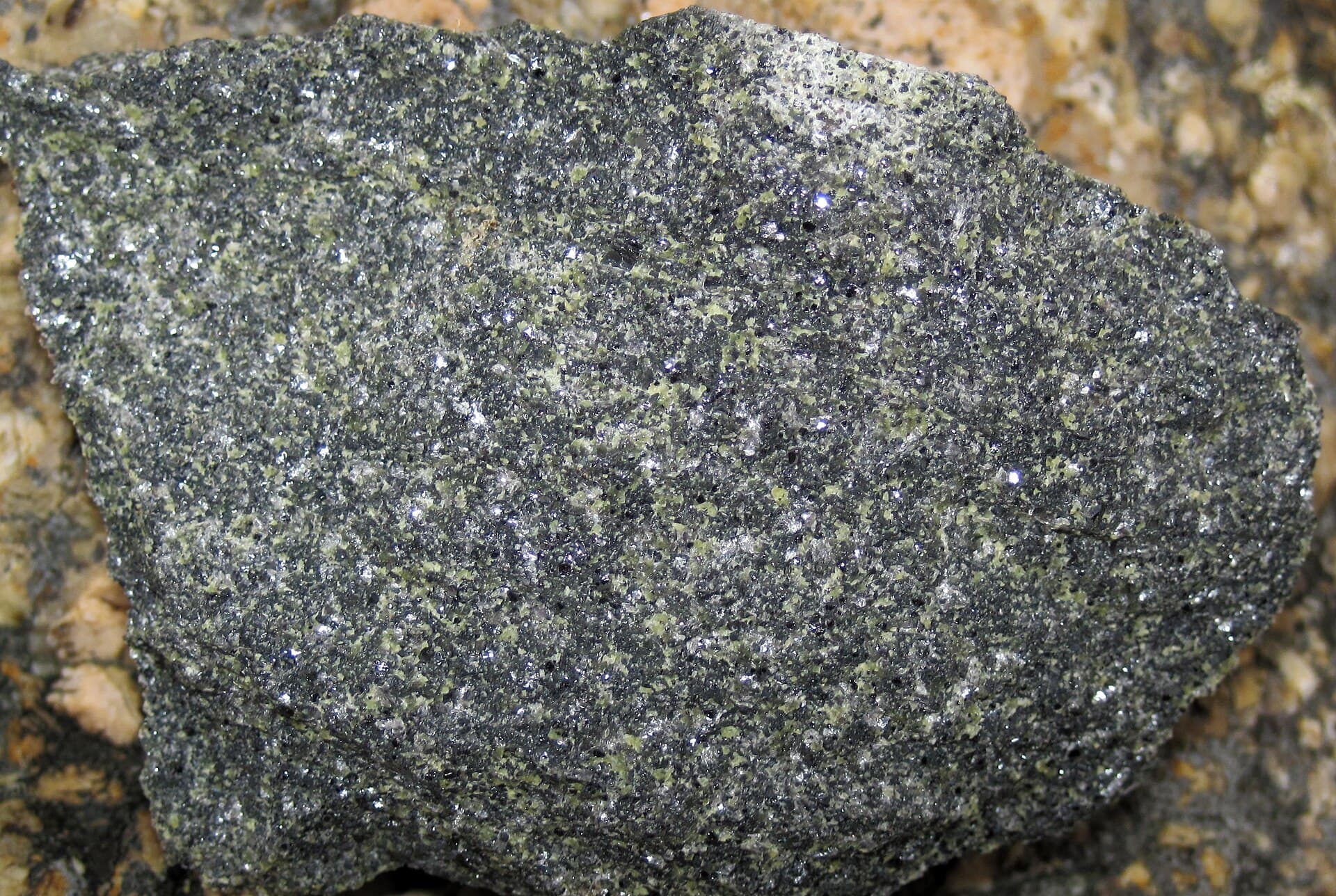 Close detail of a chromite rich rock, dark and granular with a metallic glint and green serpentine flecks