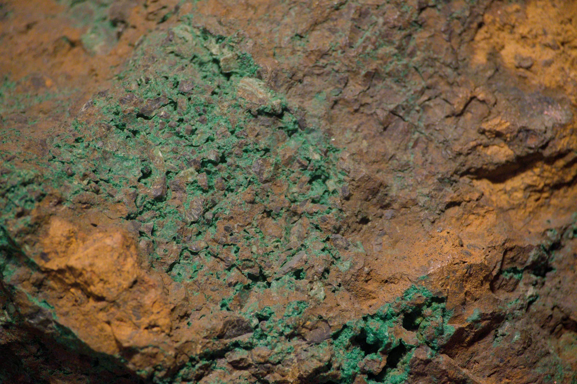 Close detail of a rock face with green copper mineralisation spread through rusty brown host rock