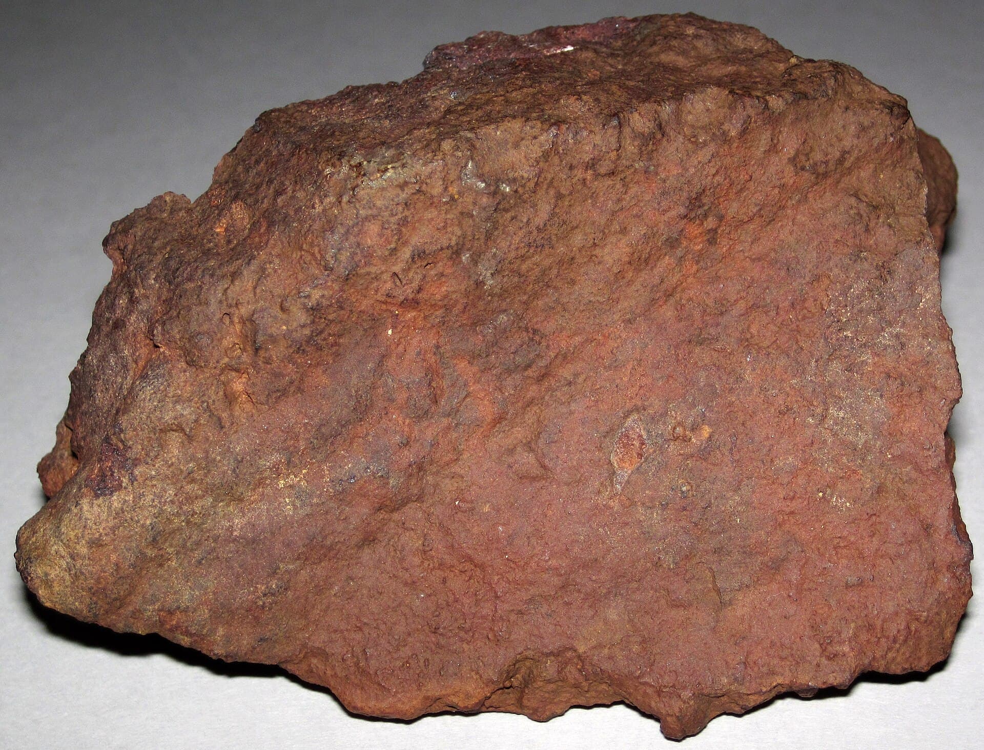 A block of hematite rich iron ore, deep rust red with a heavy dense broken surface