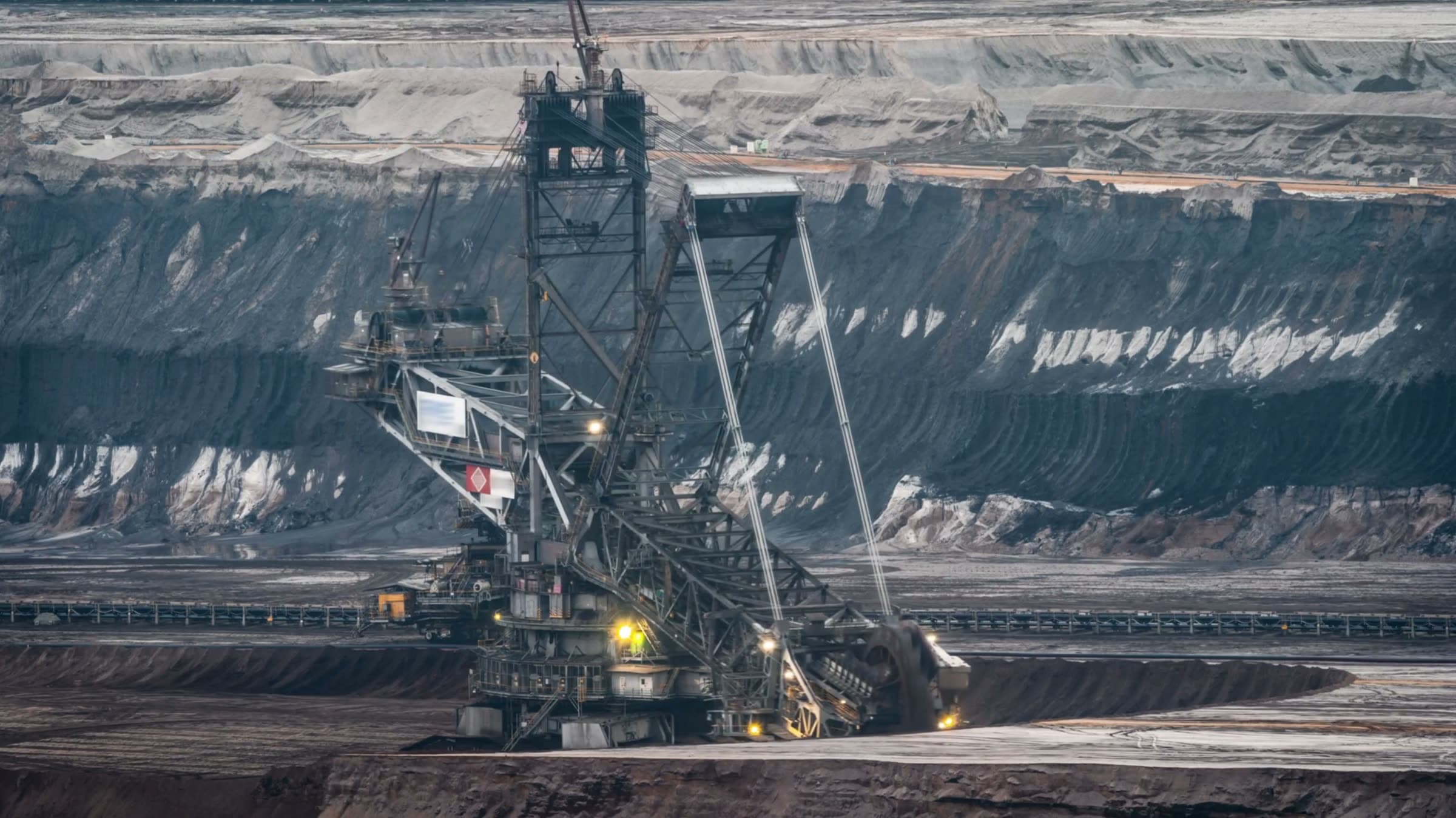 A bucket wheel excavator working the foot of a deep open pit, the cut benches of the pit wall rising behind it